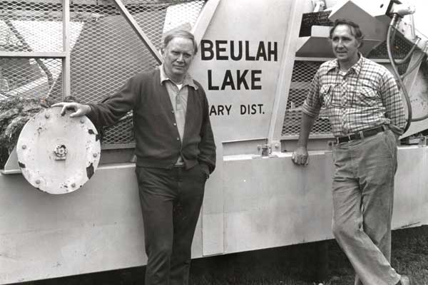 Brothers Doug & John standing next to an Aquatic Weed Harvester.